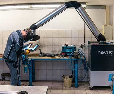 Schweißer arbeitet an einer Werkbank mit Absauganlage für Schweißrauch in einer Werkstatt