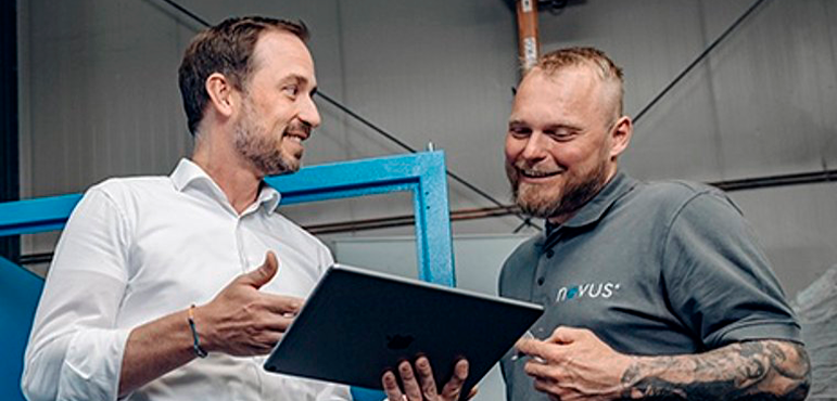 Zwei Kollegen betrachten gemeinsam ein Tablet und sprechen über Arbeitsabläufe in einer Produktionshalle