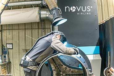 Arbeiter führt Schweißarbeiten an einem großen Metallbauteil mit industrieller Absauganlage durch